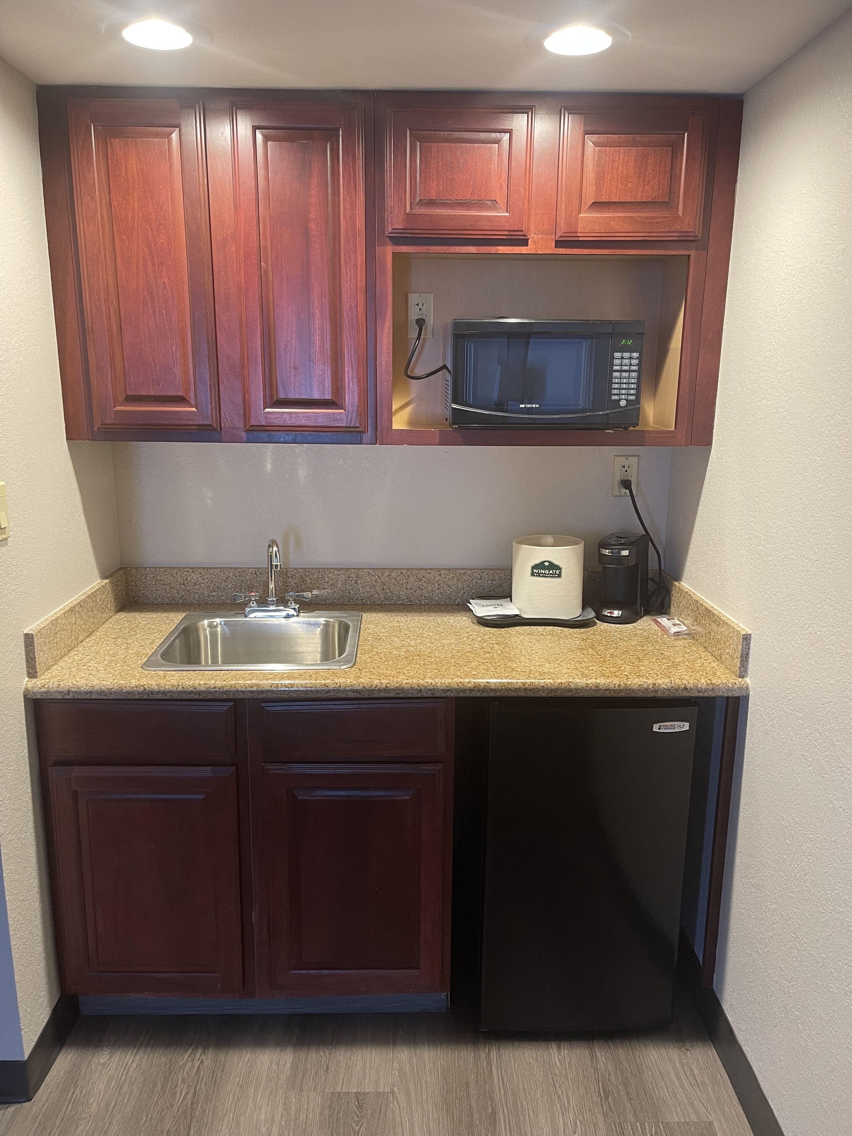 A compact kitchen with wooden cabinets, a stainless steel sink, a microwave, a coffee maker, and a dishwasher.