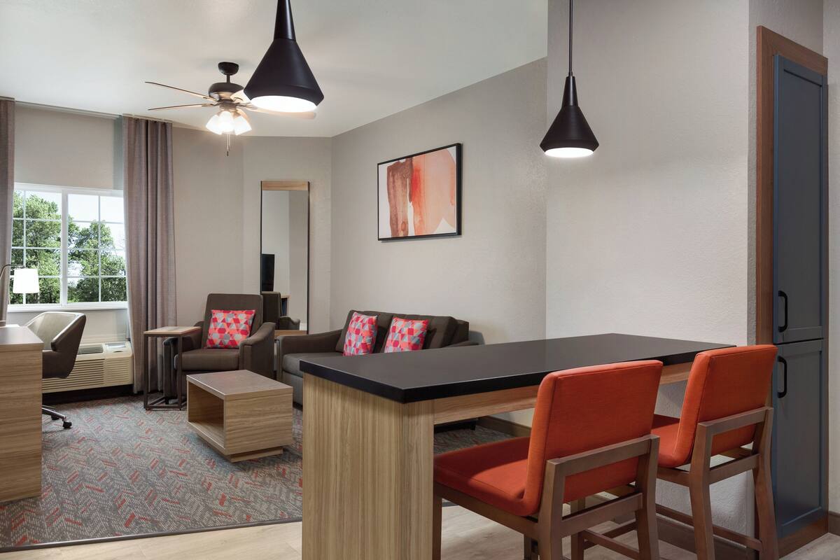 Una habitación de hotel moderna con zona de comedor, sofá, escritorio y ventilador de techo.
