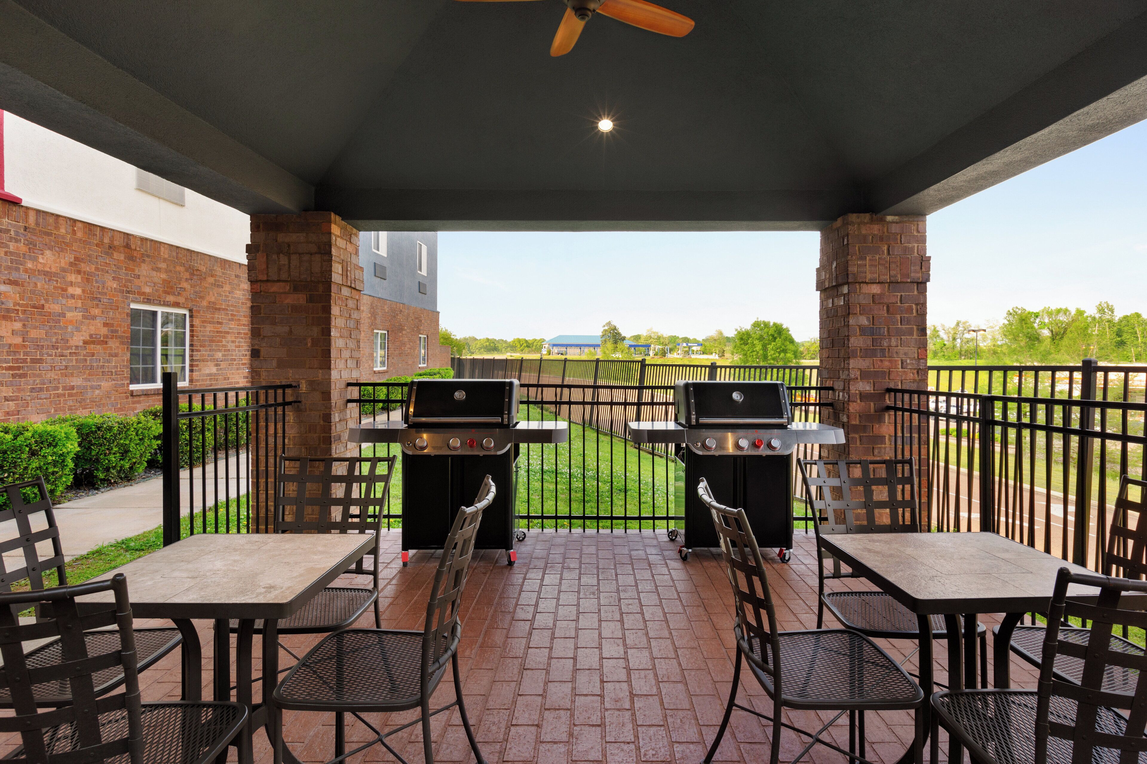 An outdoor patio with brick flooring, two barbecue grills, and metal chairs and tables.