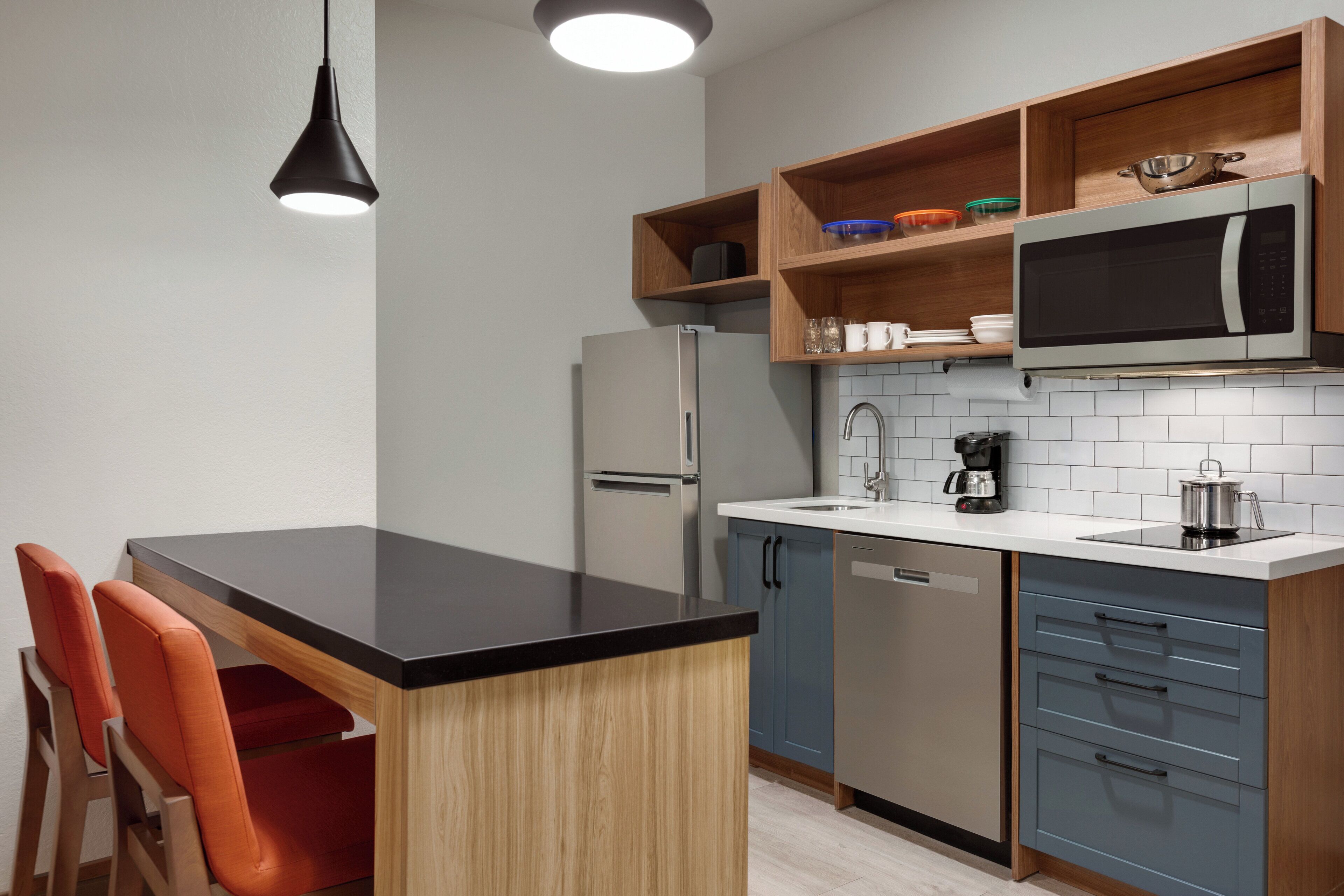 A modern kitchen with a black countertop, wooden cabinets, a built-in microwave, and a coffee maker.