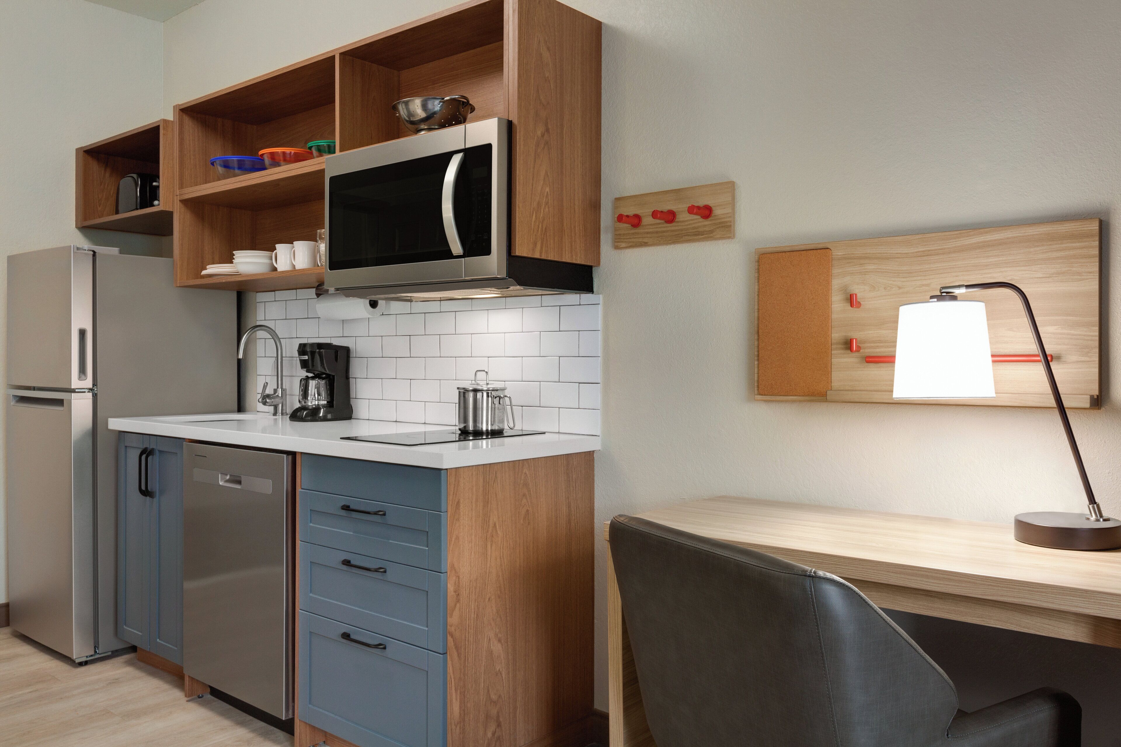 Een functionele keuken met een magnetron, koffiezetapparaat en een houten plank met servies.