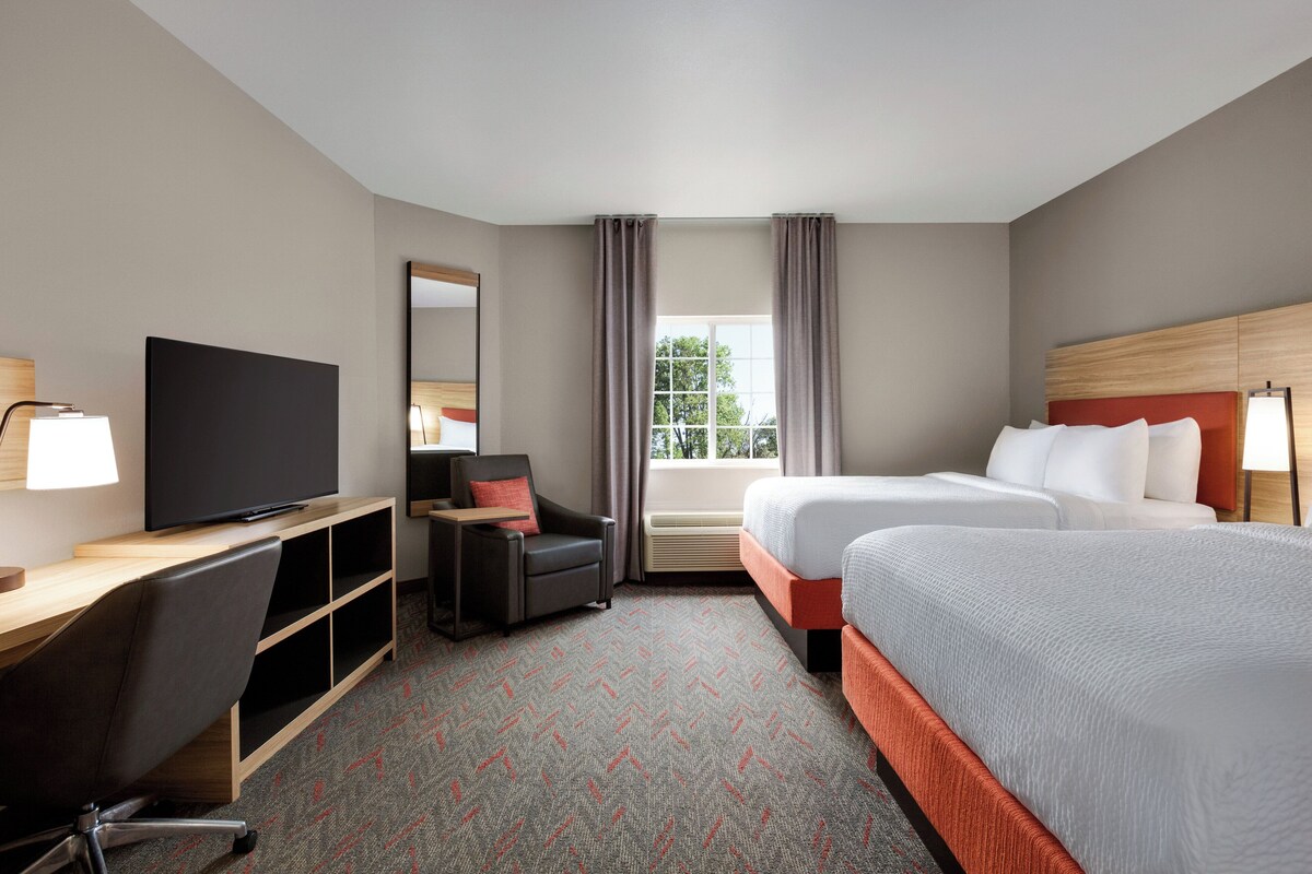 Habitación de hotel con cama, escritorio, televisor, silla y ventana con cortinas.