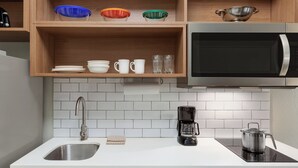 Een keuken met een RVS spoelbak, een koffiezetapparaat, een magnetron en planken met kommen en bekers.