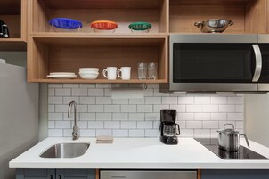 A kitchen with a stainless steel sink, a coffee maker, a microwave, and shelves with bowls and cups.