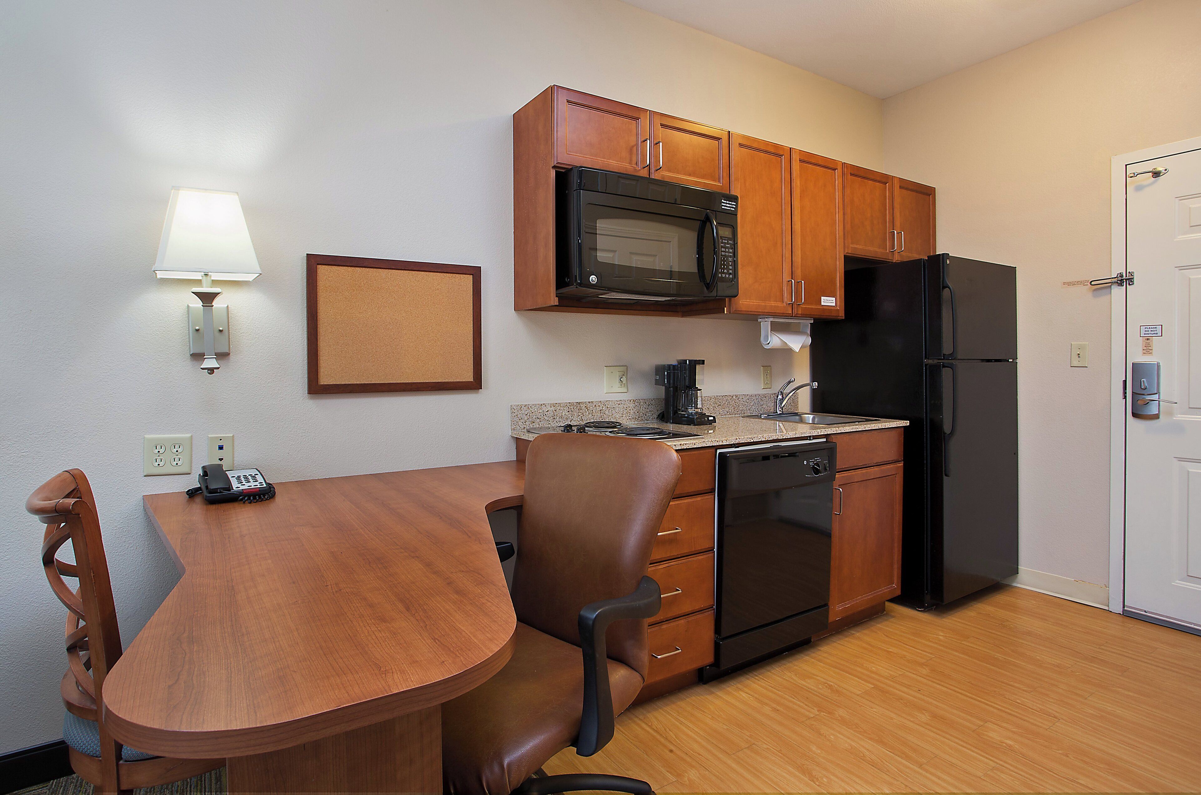 A compact kitchen with wooden cabinets, a microwave, a refrigerator, a coffee maker, and a dining table with chairs.