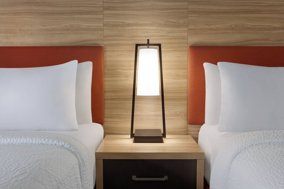 Una habitación de hotel con dos camas, una mesita de noche con lámpara y un cabecero de madera.