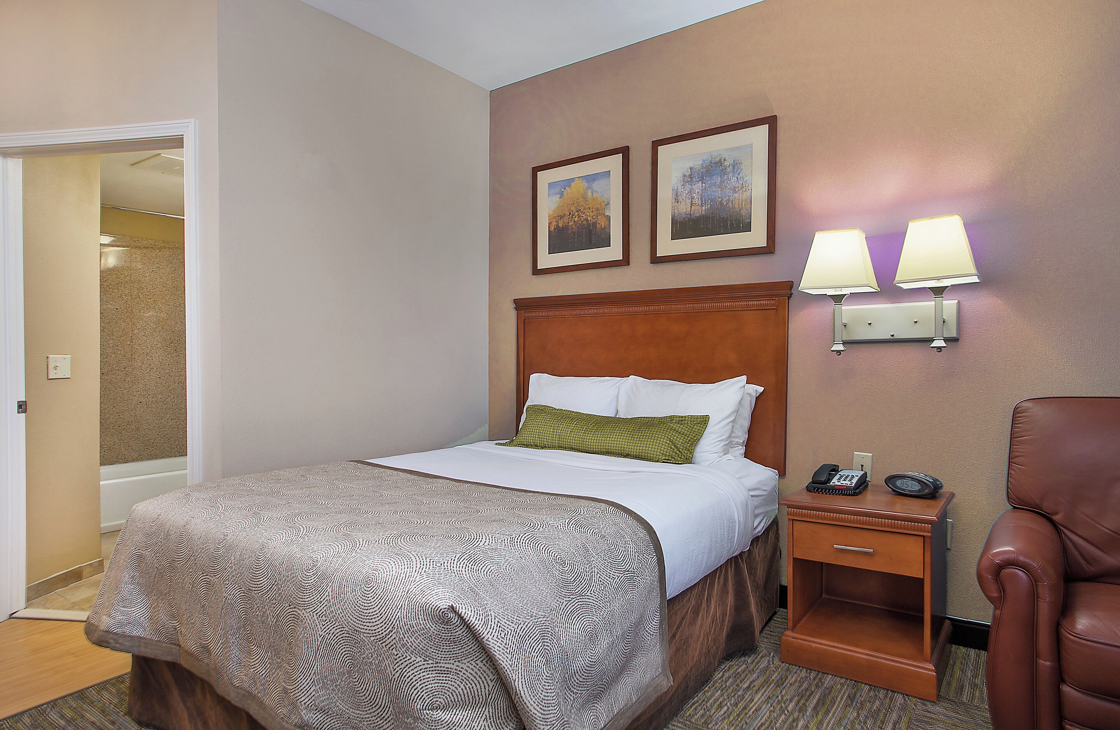 A hotel room with a bed, a nightstand, a chair, and two wall-mounted lamps.