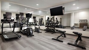Een moderne sportschool met diverse fitnessapparaten, grote spiegels en een flatscreen televisie.