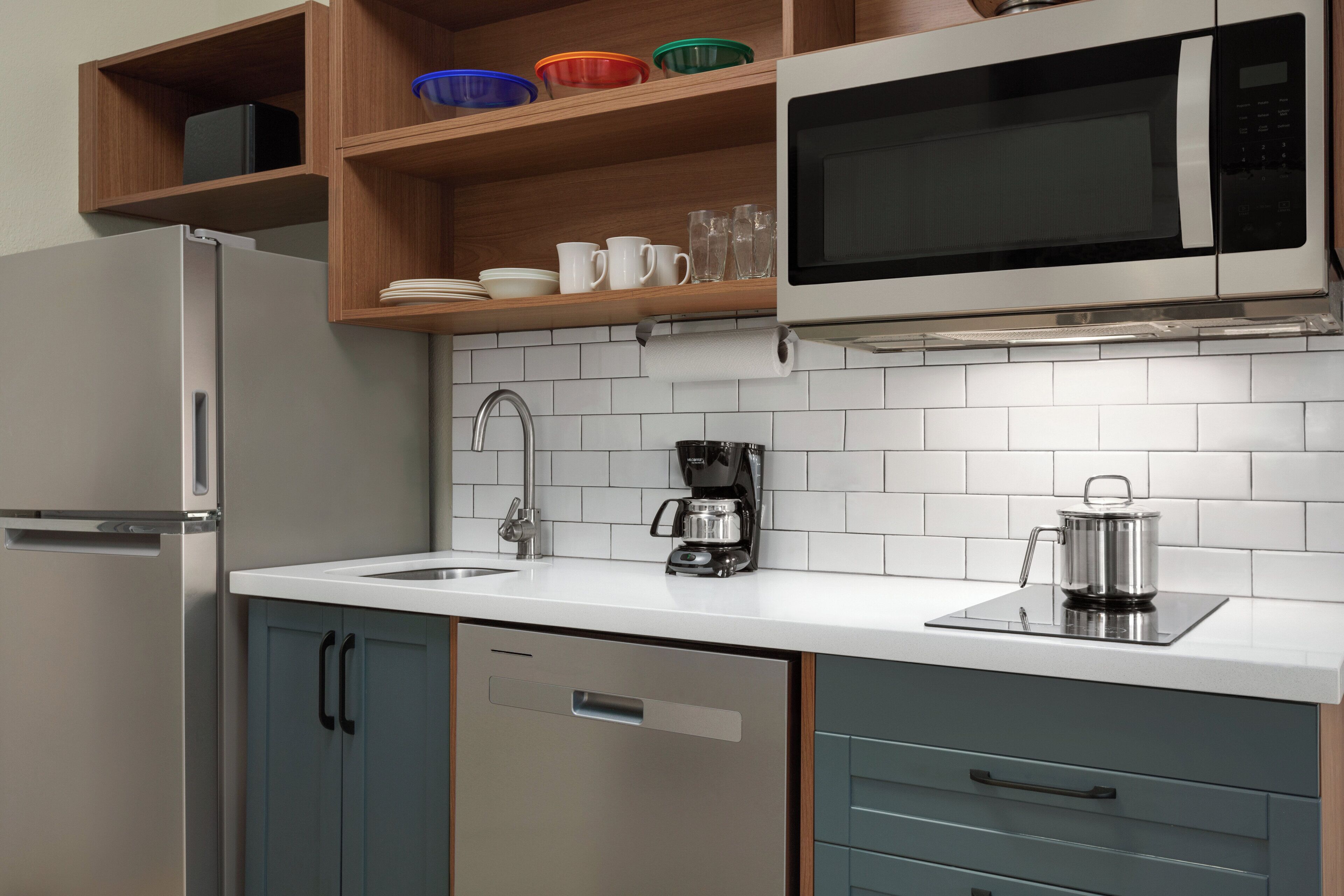 A modern kitchen with a stainless steel refrigerator, a microwave, a coffee maker, and a kettle on the countertop.
