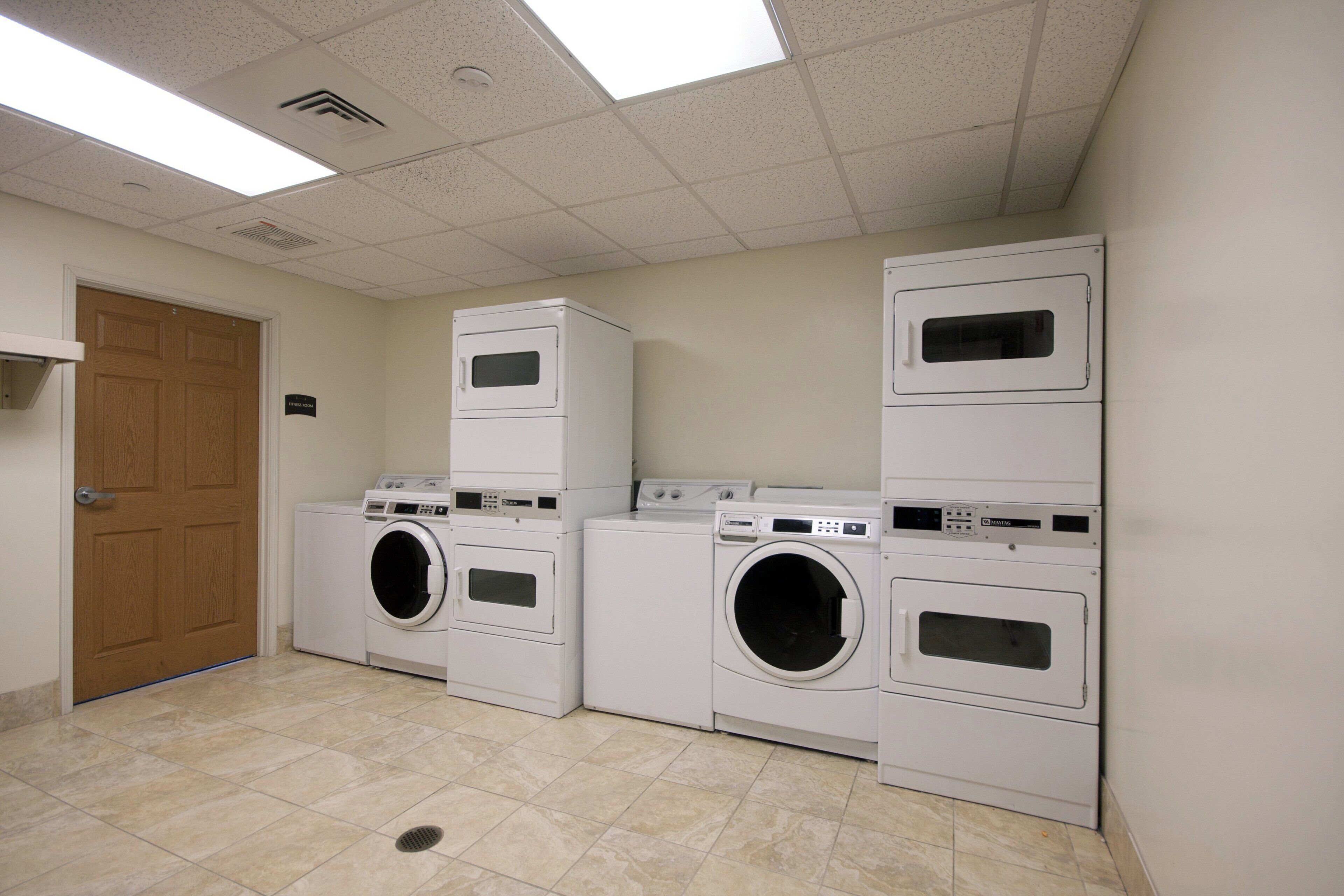 A laundry room with four stacked washing machines, a door, and a sign indicating it's a fitness room.