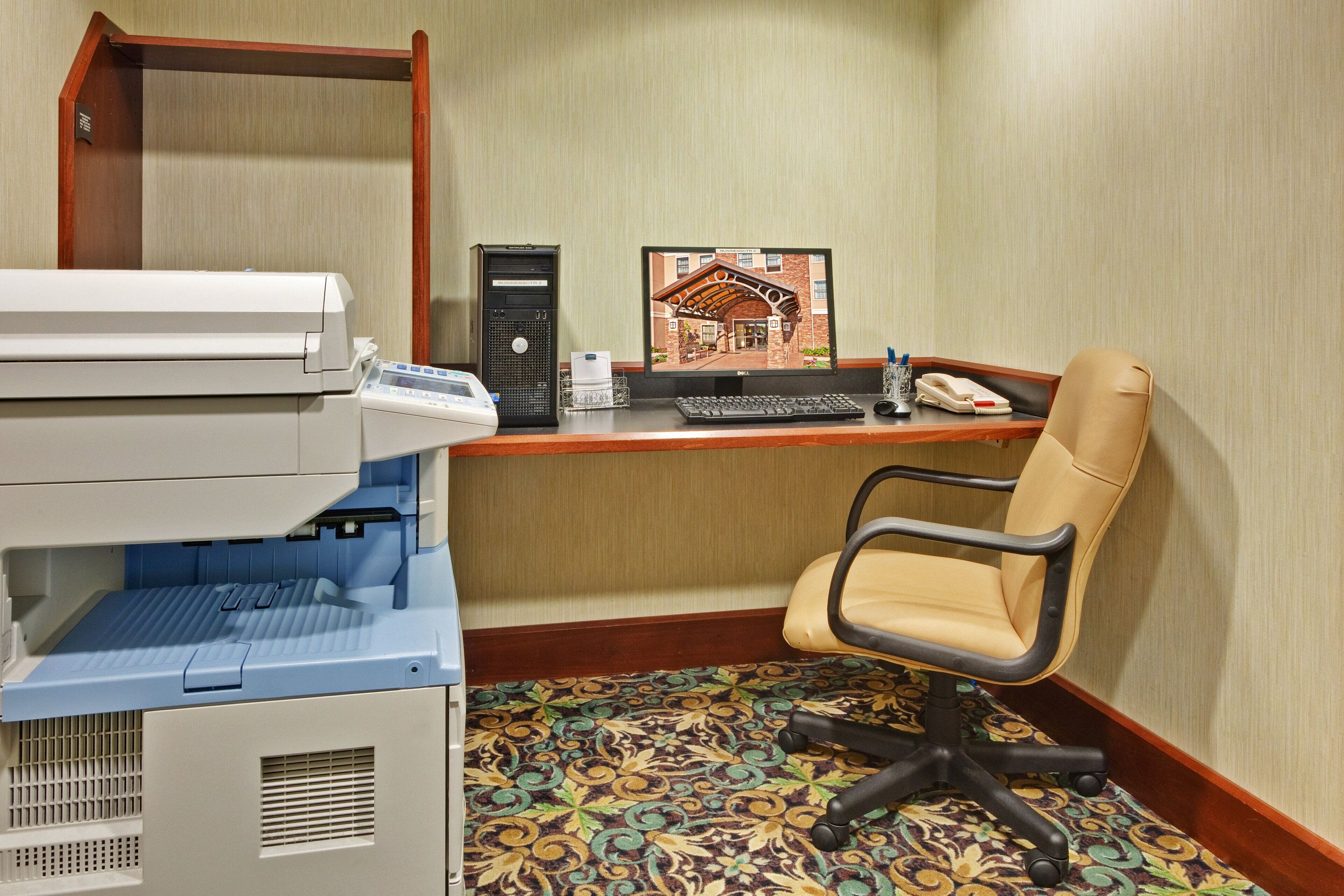 Une chambre d’hôtel équipée d’un bureau, d’un ordinateur, d’une imprimante, d’une chaise et d’une moquette à motifs.