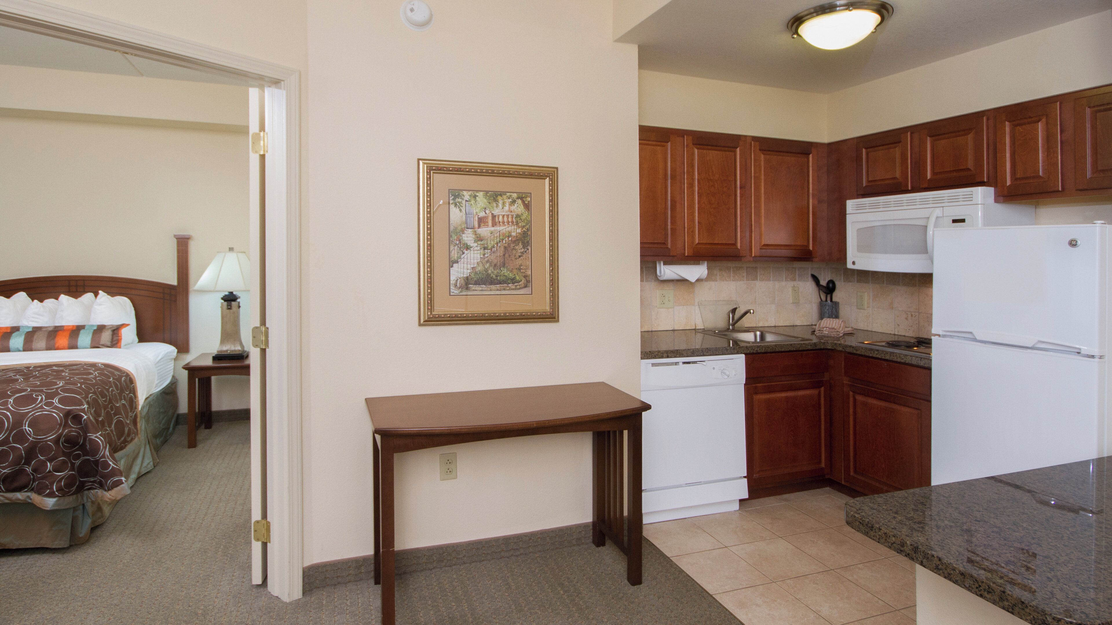 A hotel room with a bed, bedside table, lamp, and a framed picture on the wall.