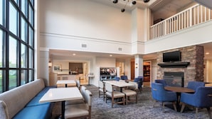 A spacious indoor area with a dining area, seating, a fireplace, and a kitchen in the background. - Staybridge Suites West Seneca by IHG (Buffalo)
