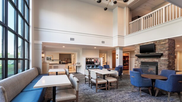 A spacious indoor area with a dining area, seating, a fireplace, and a kitchen in the background. - Staybridge Suites West Seneca by IHG (Buffalo)