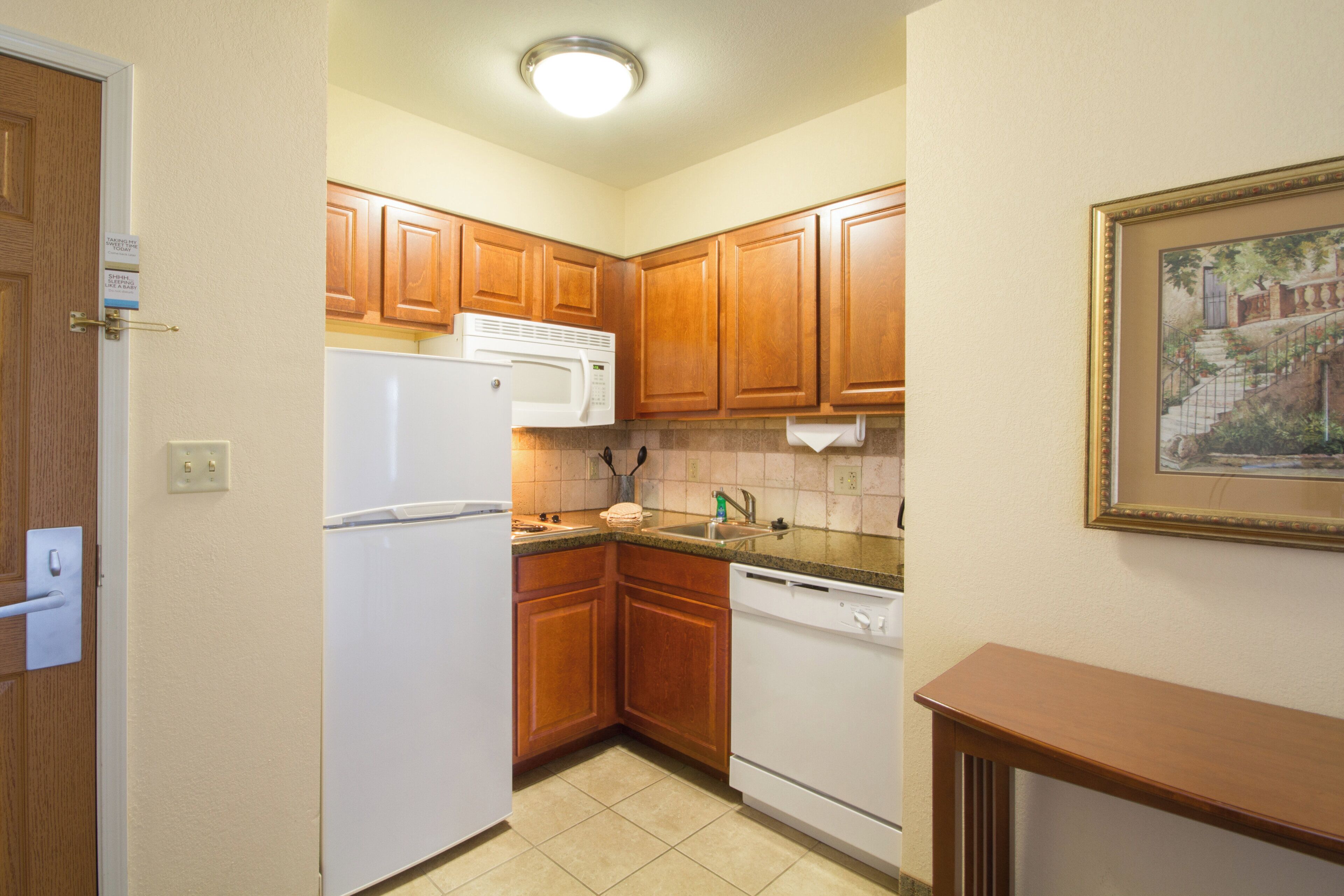 A compact kitchen with wooden cabinets, a white refrigerator, a microwave, and a dishwasher.