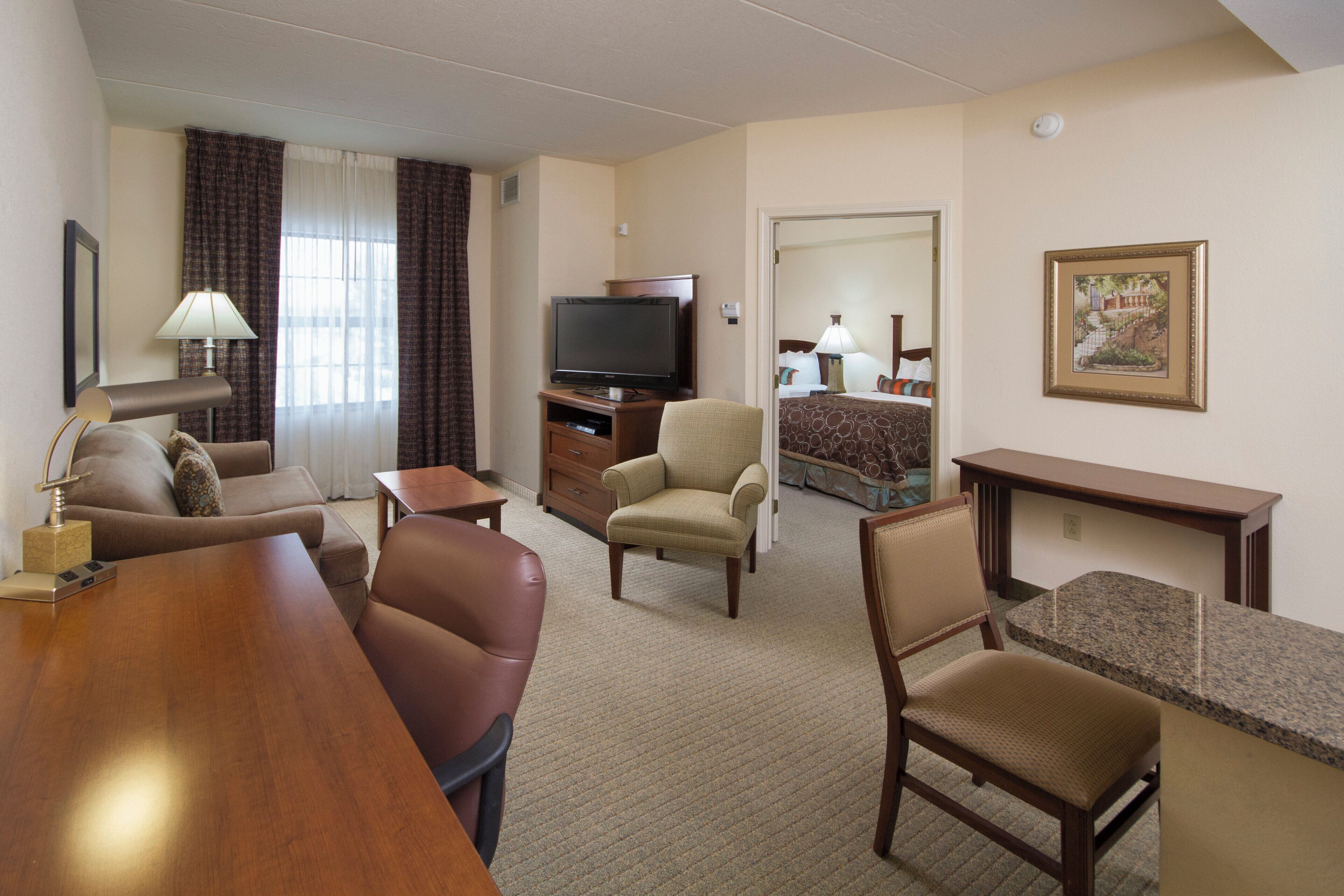 A hotel room with a living area, a television, a dining table, and a bed.