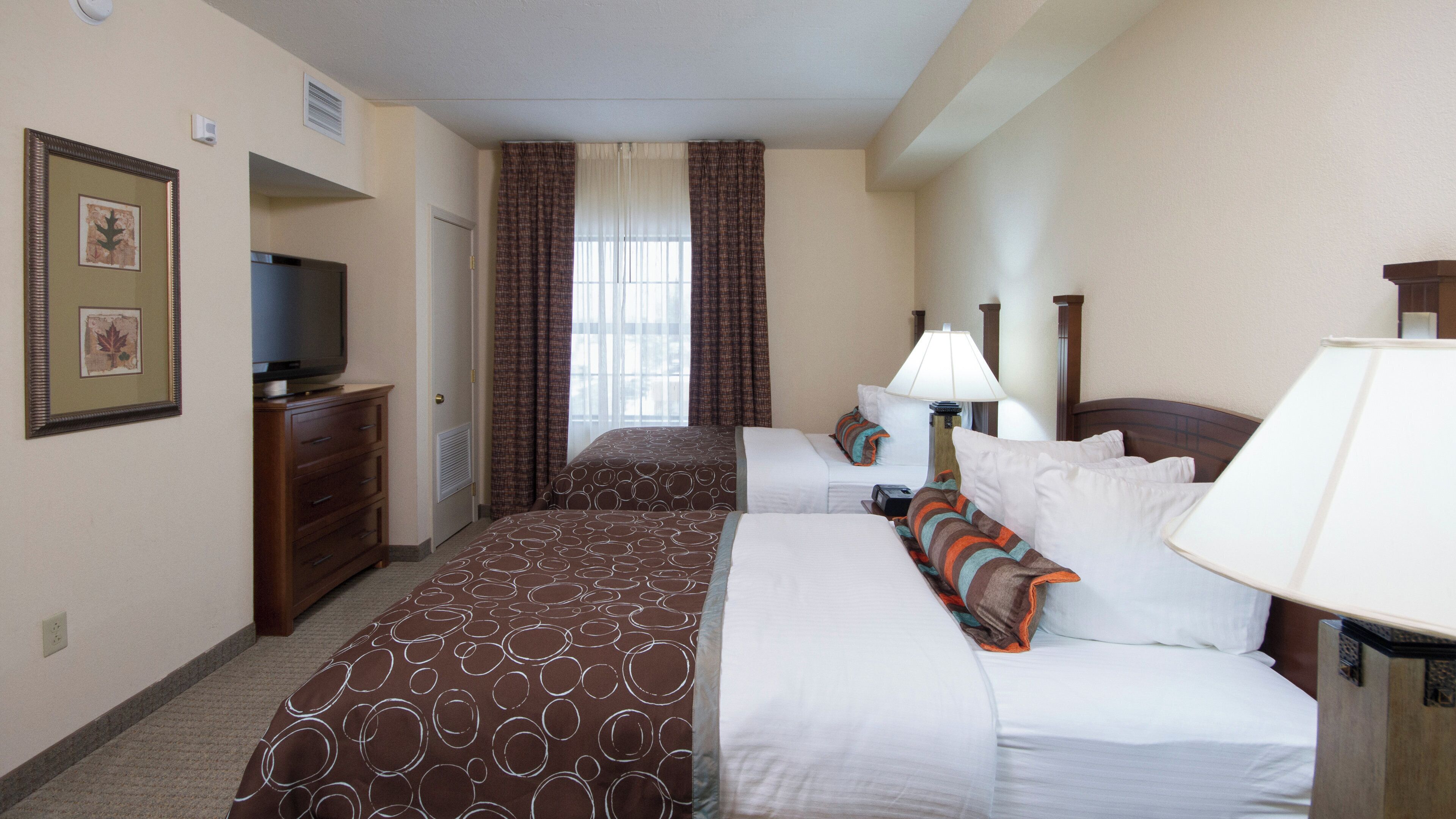 Quarto de hotel com duas camas, televisão, escrivaninha e janela com cortinas.