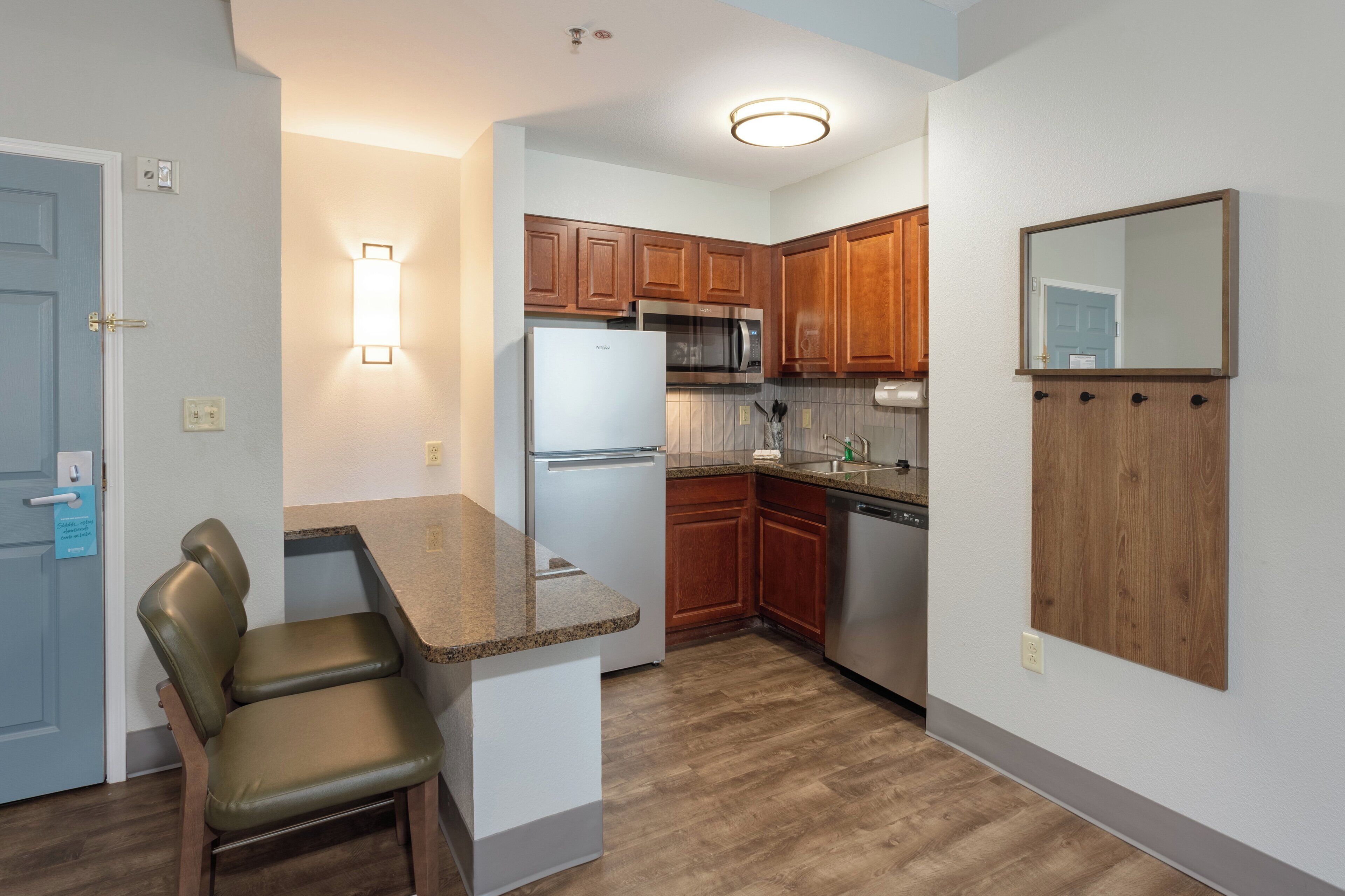 A compact kitchen with wooden cabinets, a stainless steel refrigerator, and a built-in microwave.