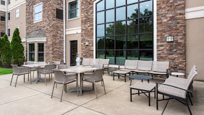 An outdoor patio with wicker furniture and a large glass window. - Staybridge Suites West Seneca by IHG (Buffalo)