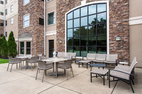 An outdoor patio with wicker furniture and a large glass window. - Staybridge Suites West Seneca by IHG (Buffalo)