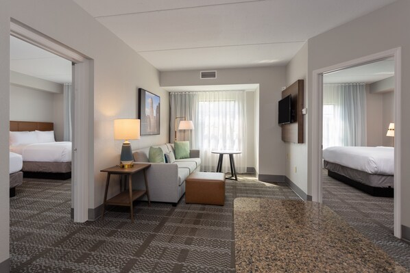 A hotel room with a bed, a sofa, a table, and a TV. - Staybridge Suites West Seneca by IHG (Buffalo)