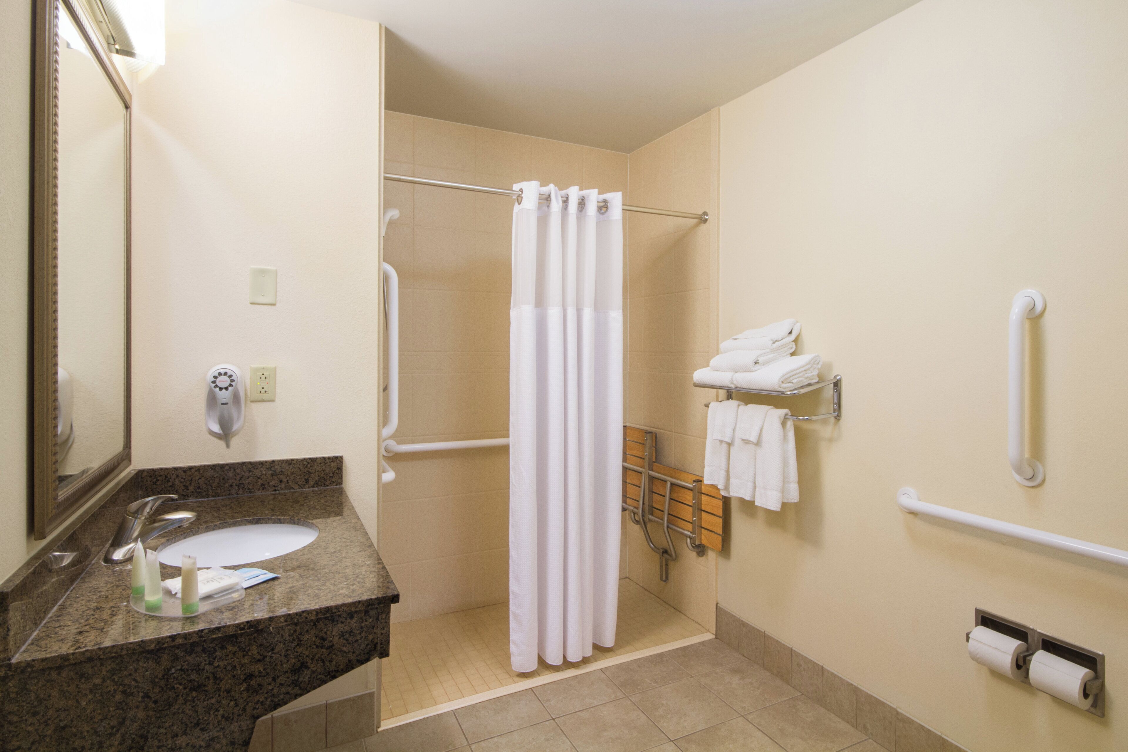 Ein Badezimmer mit Waschbecken, Spiegel, Dusche und Toilettenpapierhalter.