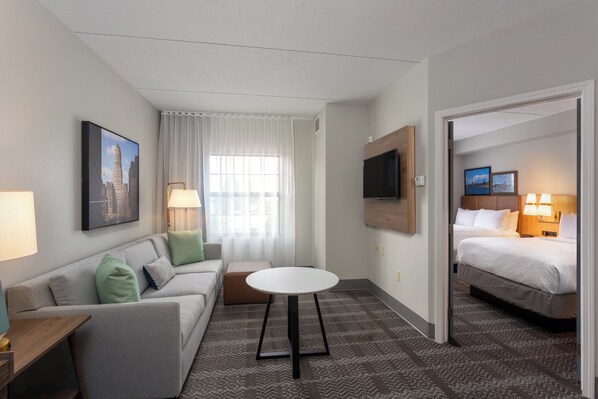 Een hotelkamer met een bed, een slaapbank, een klein tafeltje, een televisie en een raam met gordijnen.