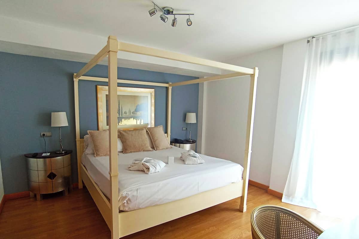 Un lit à baldaquin avec un cadre en bois, deux tables de chevet avec des lampes, un miroir au-dessus du lit et une chaise dans un coin.