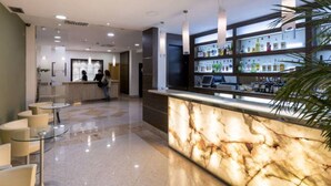 A modern hotel lobby with a marble reception desk, a bar area with shelves of liquor, and a seating area with round tables. - Hotel ITC Salamanca by Soho Boutique (Salamanca)