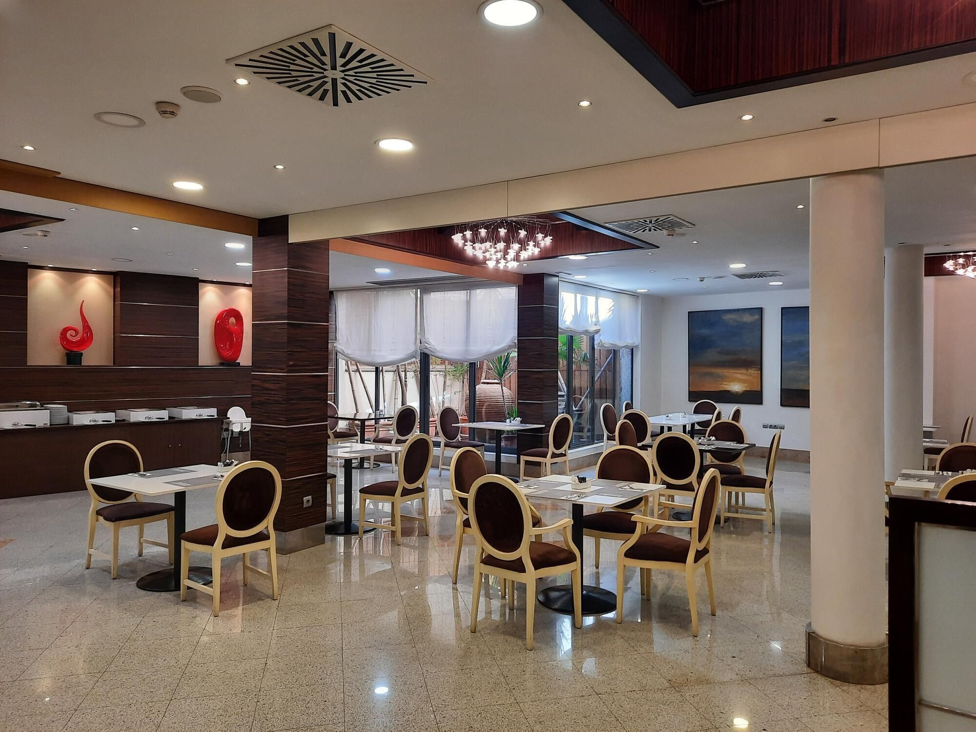 A spacious dining area with multiple tables and chairs, a modern ceiling design, and large windows allowing natural light.