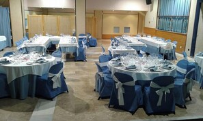 Een balzaal met ronde tafels gedekt voor een diner, elk met stoelen en servies.
