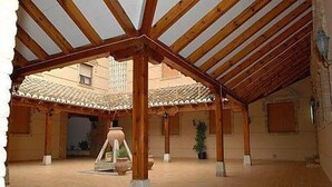 An open courtyard with wooden beams and tiled flooring, featuring potted plants and a central decorative structure. - Las Tablas (Daimiel)