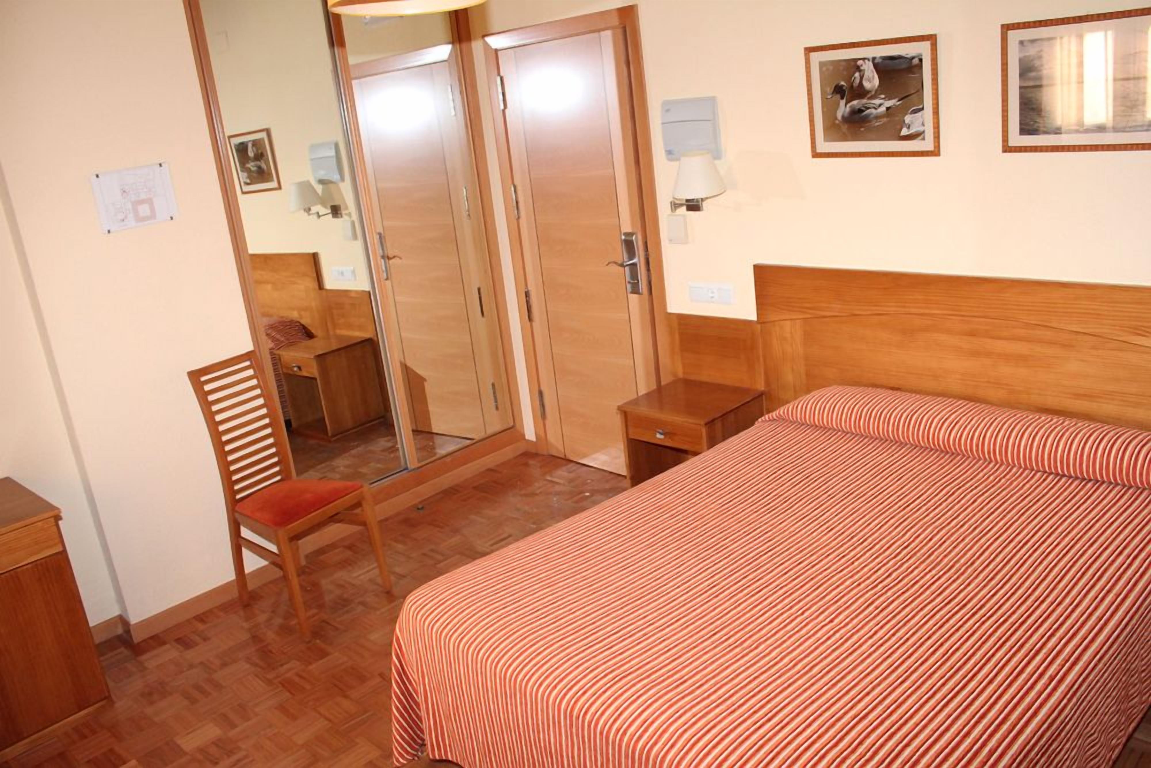 Una habitación de hotel con cama, una silla, un escritorio y un armario.