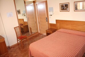 Una habitación de hotel con cama, una silla, un escritorio y un armario.