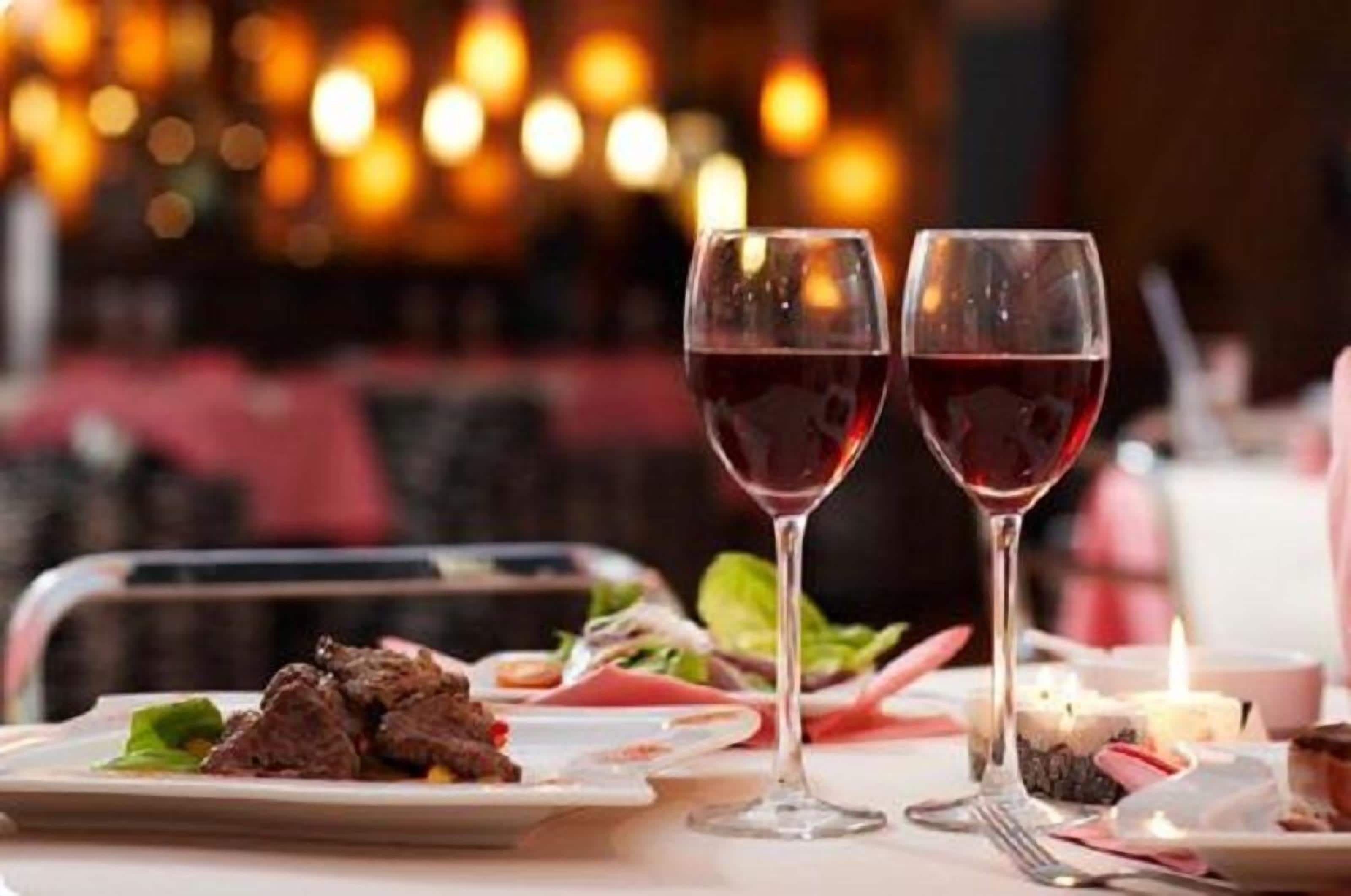 A dining table with a plate of steak and vegetables, two glasses of red wine, and a candle.