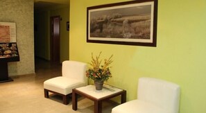 Ein Empfangsbereich mit zwei weißen Sesseln, einem kleinen Tisch mit Blumenvase und einem gerahmten Landschaftsbild an der Wand.