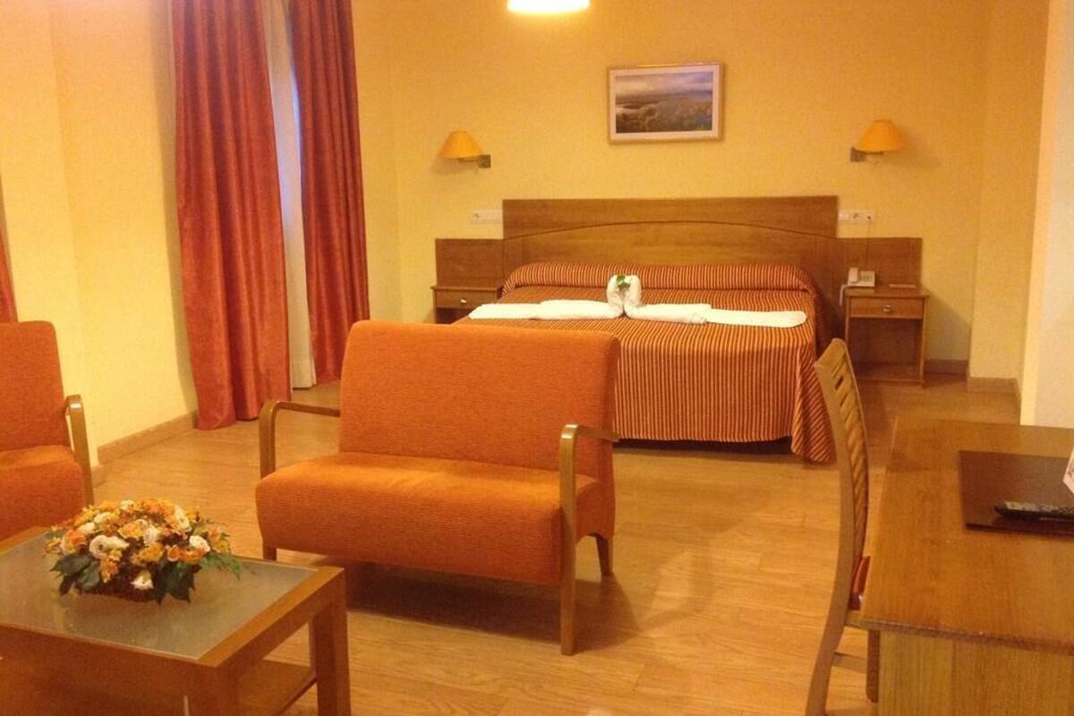 Ett hotellrum med en säng, två sängbord, ett skrivbord och två stolar.