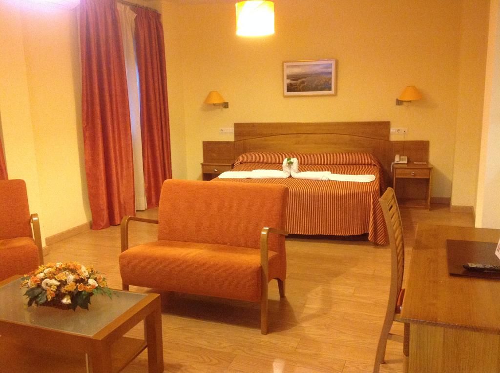 Una habitación de hotel con una cama, dos mesitas de noche, un escritorio y dos sillas.