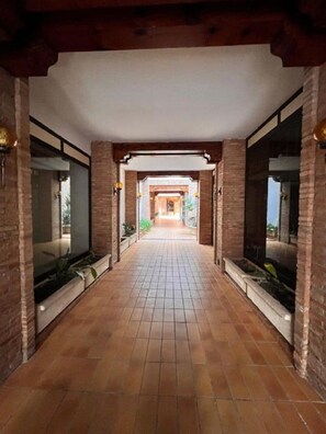 A corridor with tiled flooring, brick walls, and large windows on both sides. - Las Tablas (Daimiel)