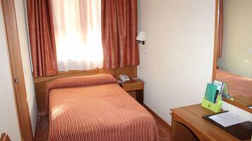 Ein Hotelzimmer mit einem Bett, einem Nachttisch mit Lampe, einem Spiegel und einem Schreibtisch mit Stuhl.