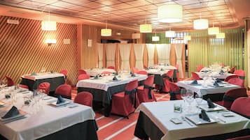 Un restaurant amb diverses taules preparades per sopar, cadascuna amb estovells blancs i caires vermells.