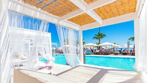 A poolside lounge with white canopies, a pool, and palm trees in the background. - Silver Sands Beach Hotel (Paralimni)