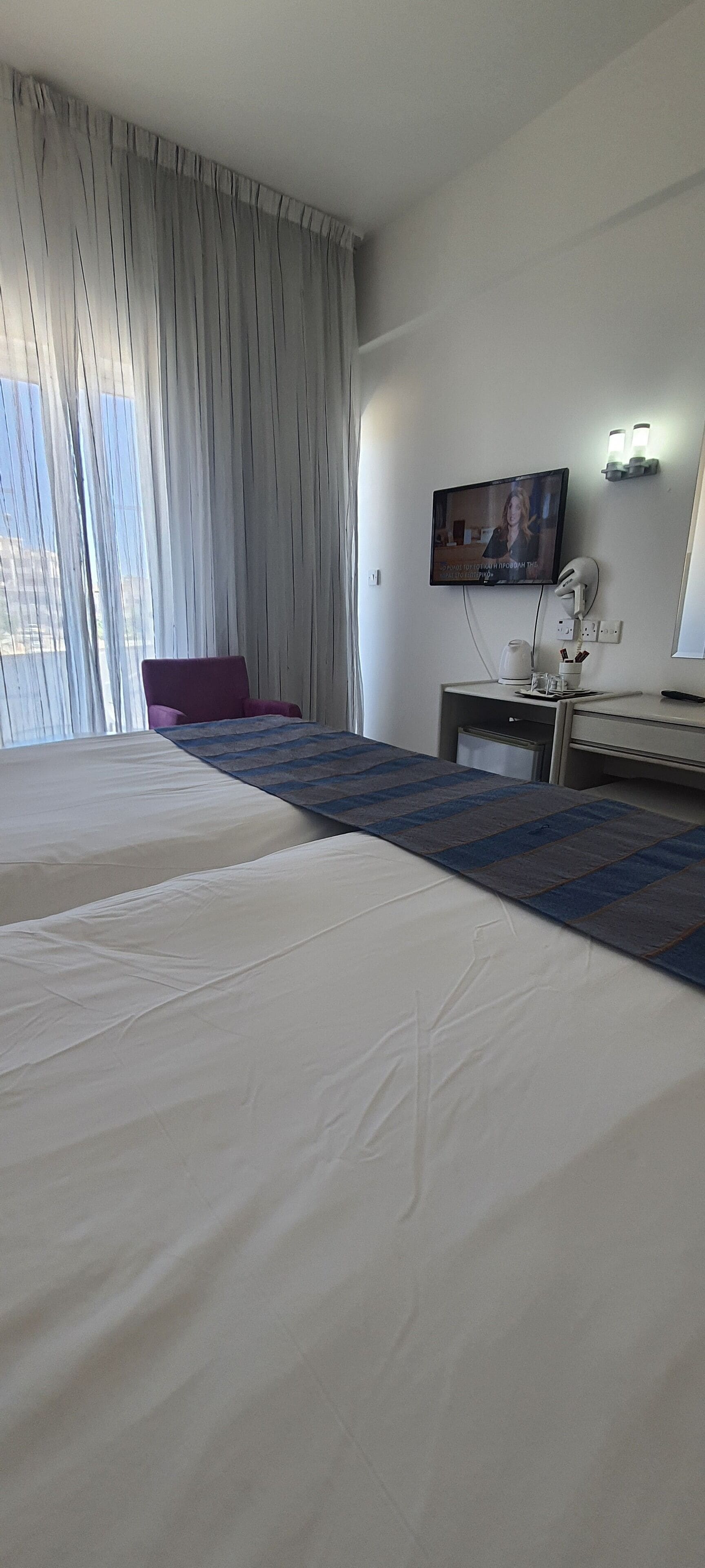 A hotel room with two beds, a TV, a desk with a lamp, and a window with curtains.