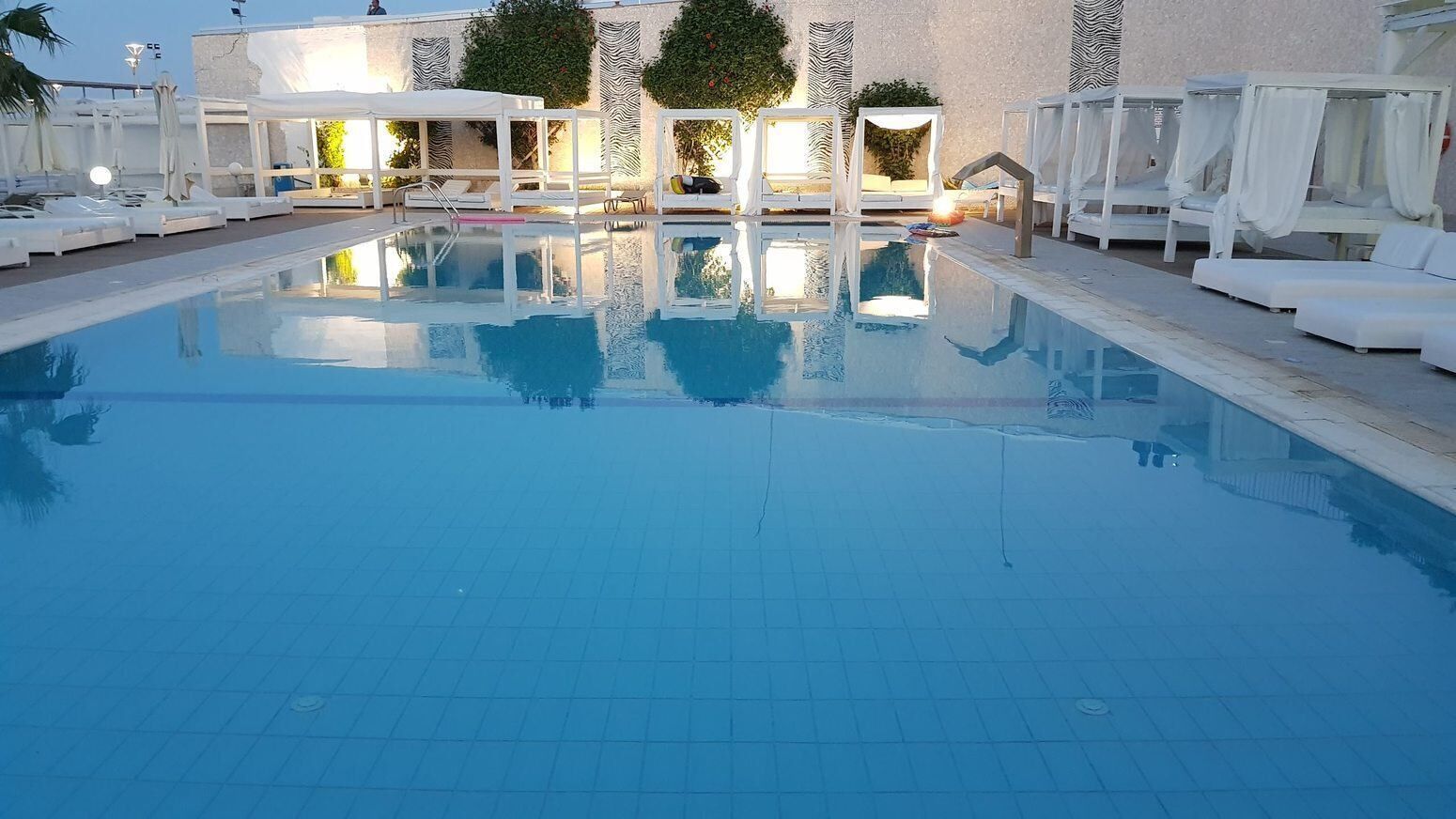 Una piscina con sillas de descanso blancas y sombrillas, rodeada por un edificio con paredes con diseños y vegetación.