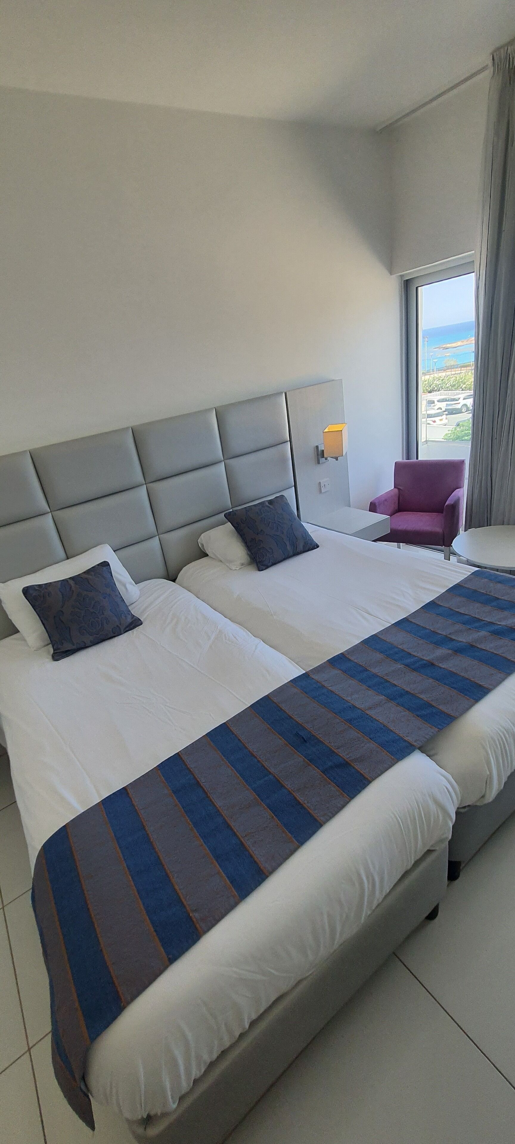 Una habitación de hotel con una cama grande, un cabecero, una ventana con cortinas y una silla.