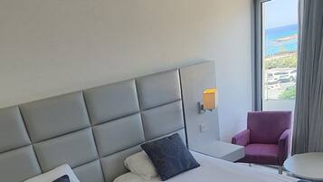 Una habitación de hotel con una cama grande, un cabecero, una ventana con cortinas y una silla.