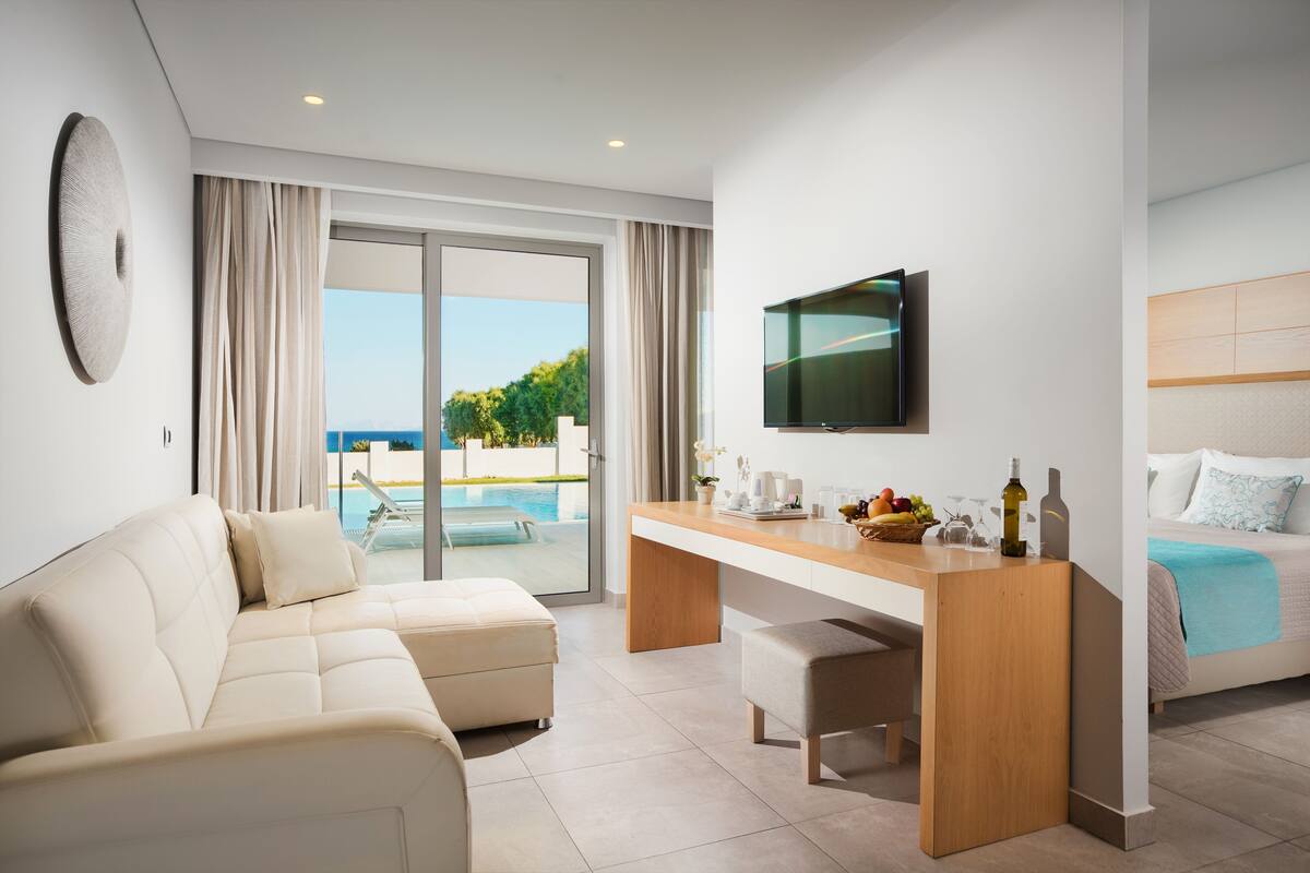 A modern hotel room with a sofa, a wooden desk, a TV, and a bed.