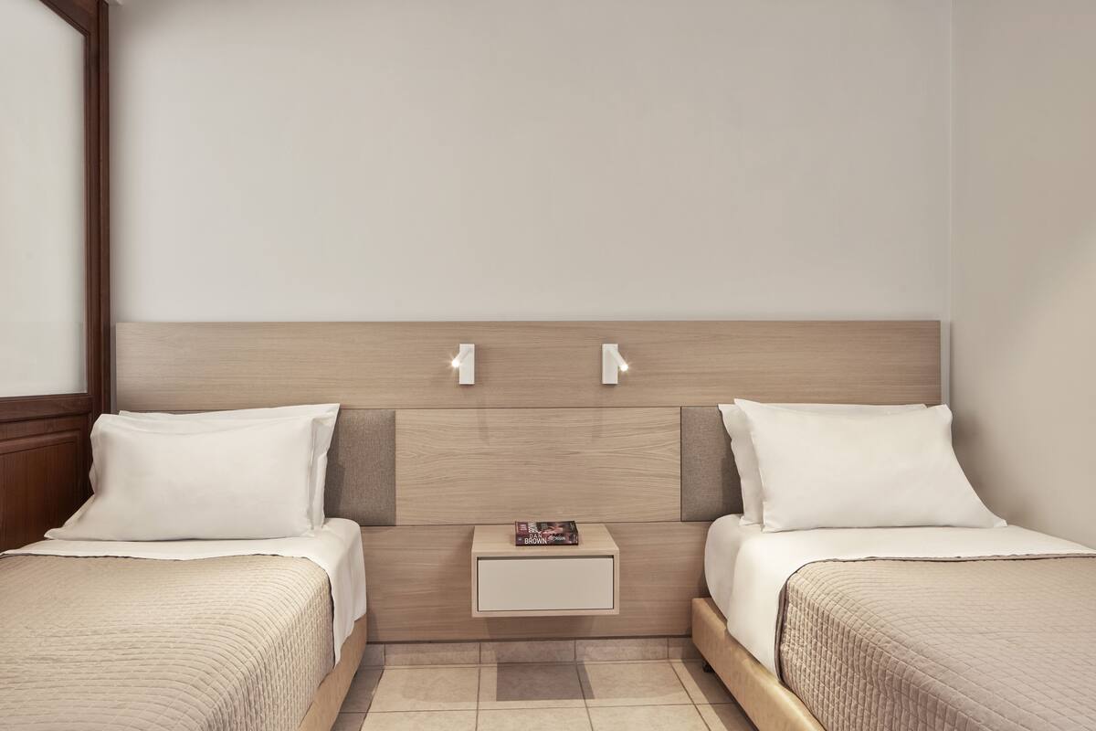 A hotel room with two beds, a nightstand, and a wall-mounted light fixture.