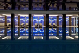 A modern indoor pool area with lounge chairs and a reflective floor.
