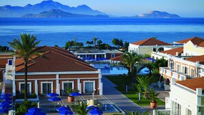 Un hotel sulla costa con piscina, ombrelloni blu e vista sul mare e sulle montagne.